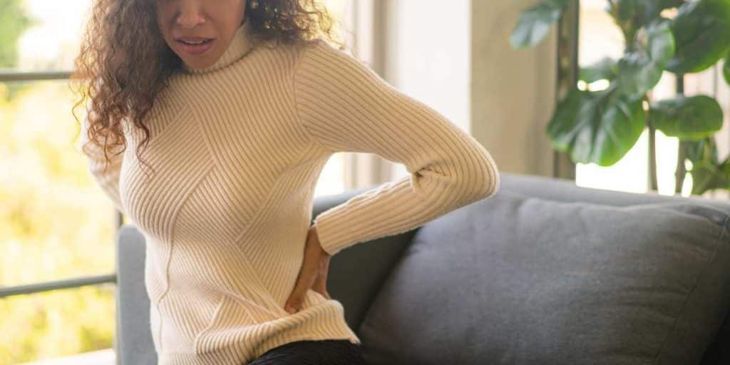 mulher com osteofitose segura na coluna e faz cara de dor