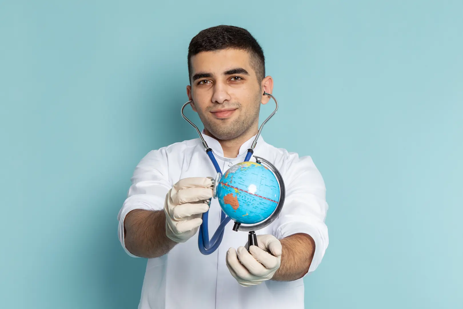 M&eacute;dico jovem com estetosc&oacute;pio sorrindo enquanto examina uma miniatura do globo terrestre - Profissional humanit&aacute;rio buscando participar do programa Mais M&eacute;dicos.