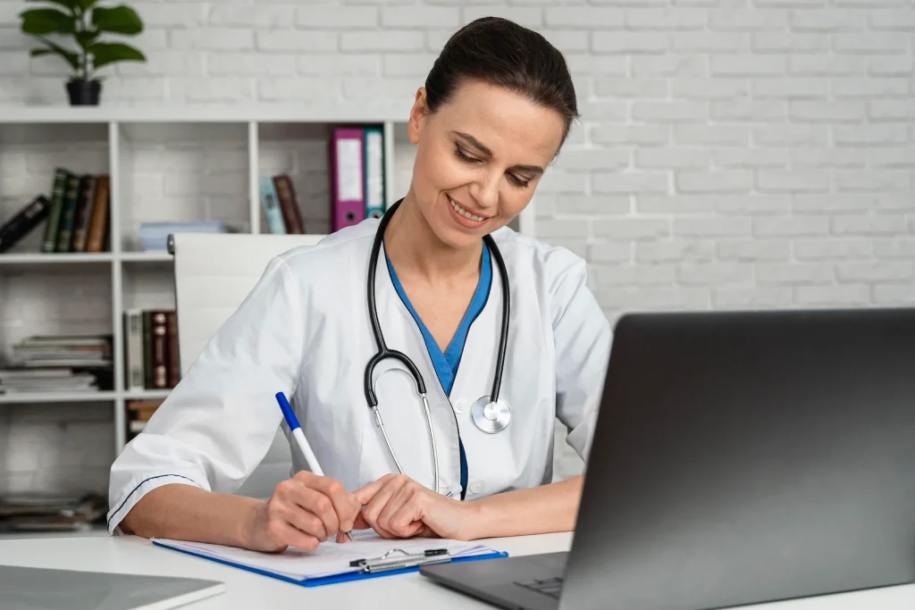 Médica estudando com o notebook enquanto faz anotações em um caderno.