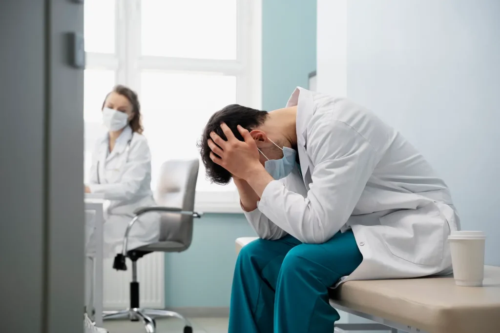 Médico usando máscara com sintomas de irritabilidade e isolamento, comuns na Síndrome de Burnout devido a má gestão hospitalar.