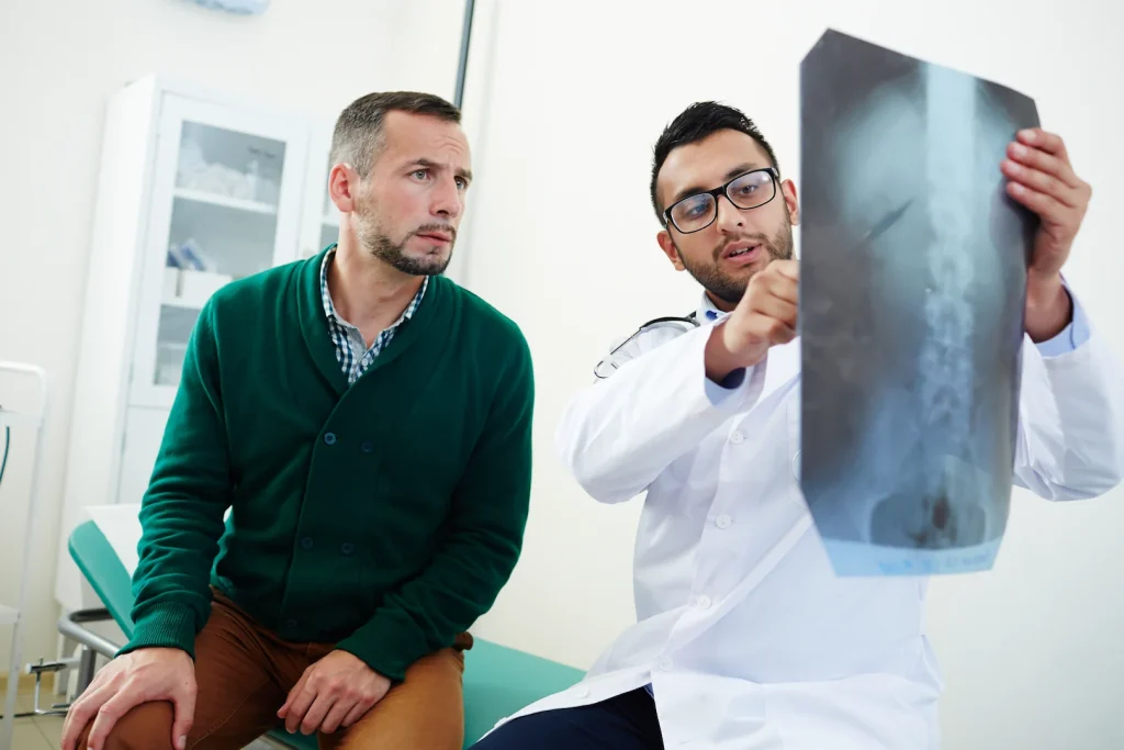 Médico explica ao paciente de tromboembolia pulmonar resultado de raio-x do pulmão. Paciente e radiologista estão em consultório especializado.