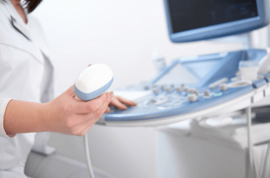 Profissional de sa&uacute;de segurando um transdutor de ultrassom ao lado de um aparelho de ultrassonografia.