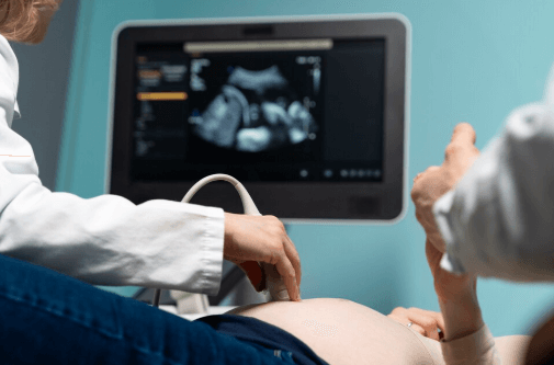A imagem mostra um profissional de sa&uacute;de realizando um exame de ultrassonografia em uma pessoa gr&aacute;vida.