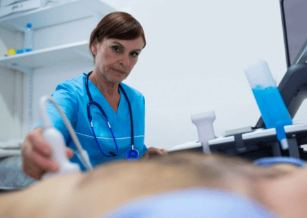A imagem mostra uma profissional de sa&uacute;de realizando uma ecocardiografia em um paciente deitado, provavelmente no pronto-socorro ou em ambiente hospitalar.
