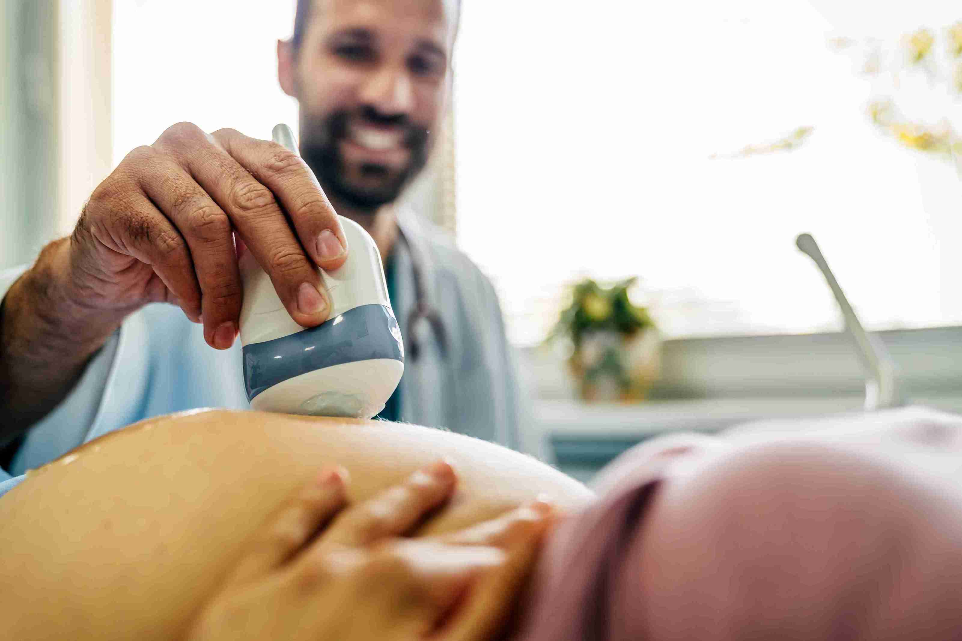 M&eacute;dico realizando ultrassonografia em gestante deitada, utilizando transdutor no abdome para avalia&ccedil;&atilde;o fetal no segundo trimestre.