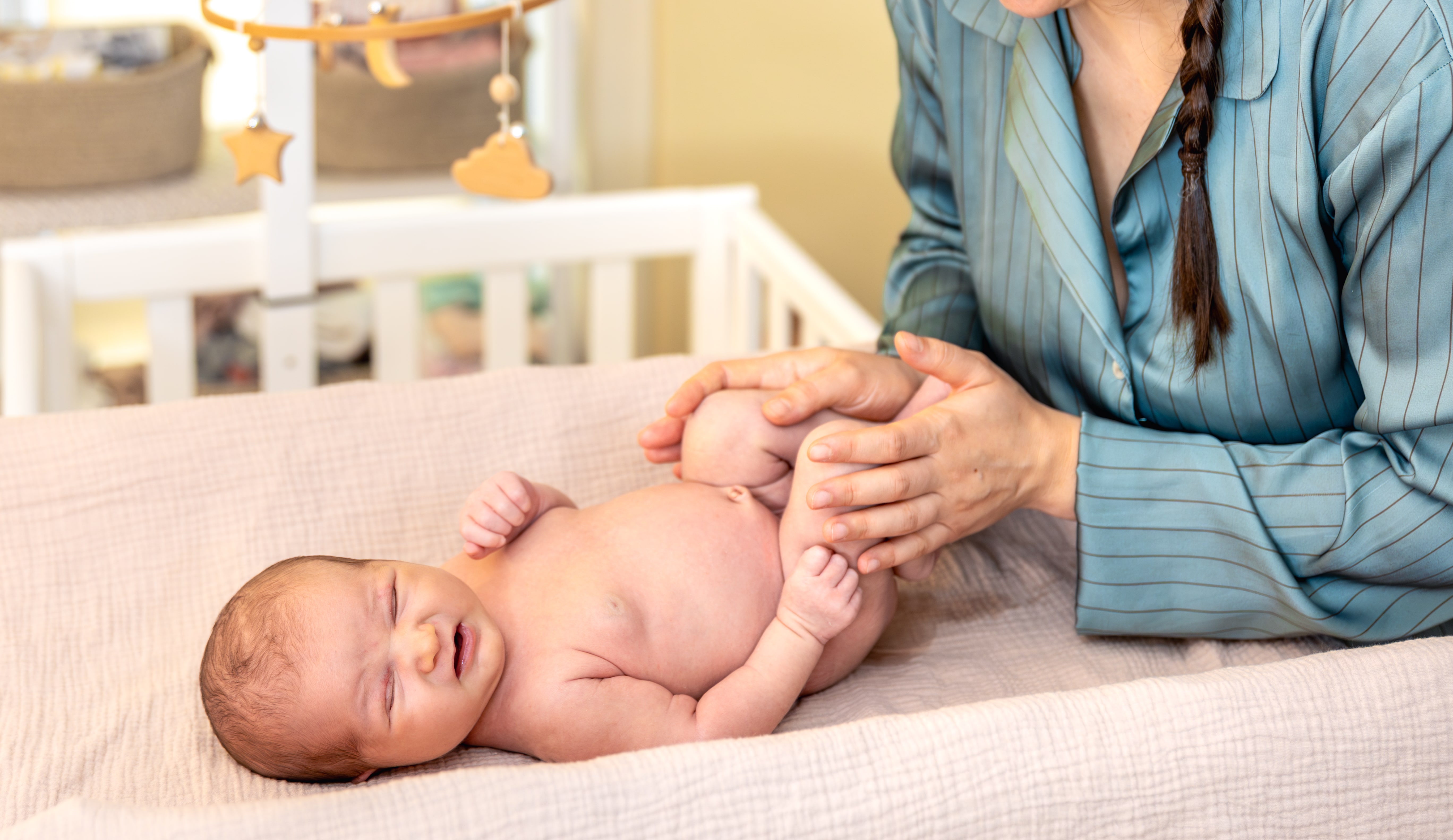 M&atilde;e segurando as pernas de um beb&ecirc; deitado em uma superf&iacute;cie acolchoada, realizando movimento que pode estar relacionado a exame de displasia do quadril em rec&eacute;m-nascidos.