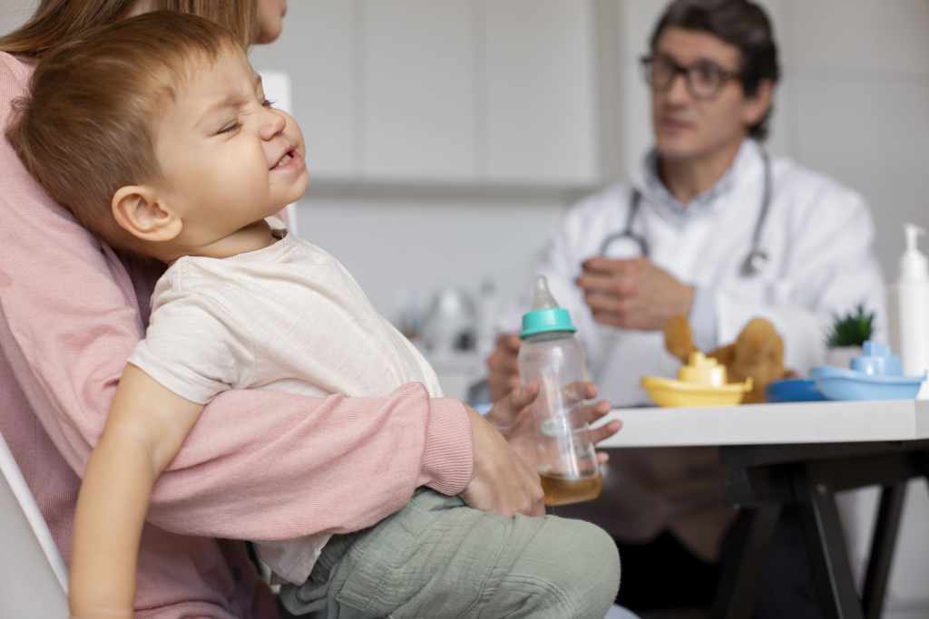 Criança com expressão de dor abdominal no colo da mãe durante consulta pediátrica, simbolizando avaliação médica de doenças gastrointestinais em crianças.