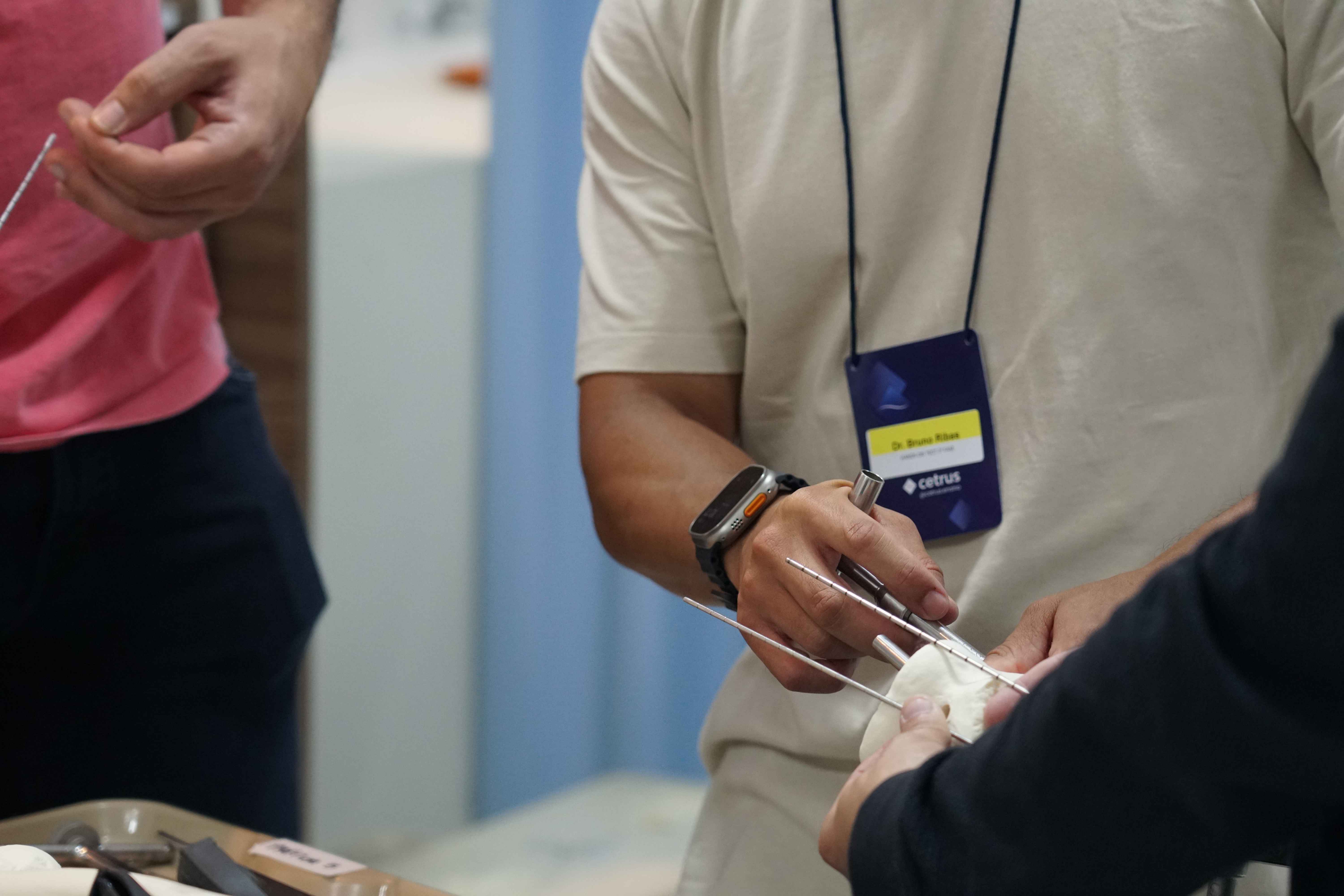 Na imagem, v&ecirc;-se um treinamento pr&aacute;tico em ambiente educacional: um profissional com crach&aacute; do Cetrus manipula instrumentos cir&uacute;rgicos sobre um modelo anat&ocirc;mico, enquanto outros participantes observam. A cena ilustra uma esta&ccedil;&atilde;o Hands-On de habilidades cir&uacute;rgicas.