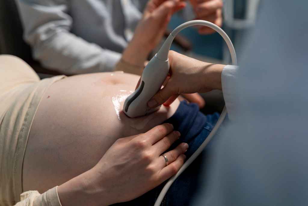 Ecocardiografia fetal realizada em gestante, com transdutor de ultrassom posicionado sobre o abdome para avalia&ccedil;&atilde;o do cora&ccedil;&atilde;o fetal durante exame pr&eacute;-natal.