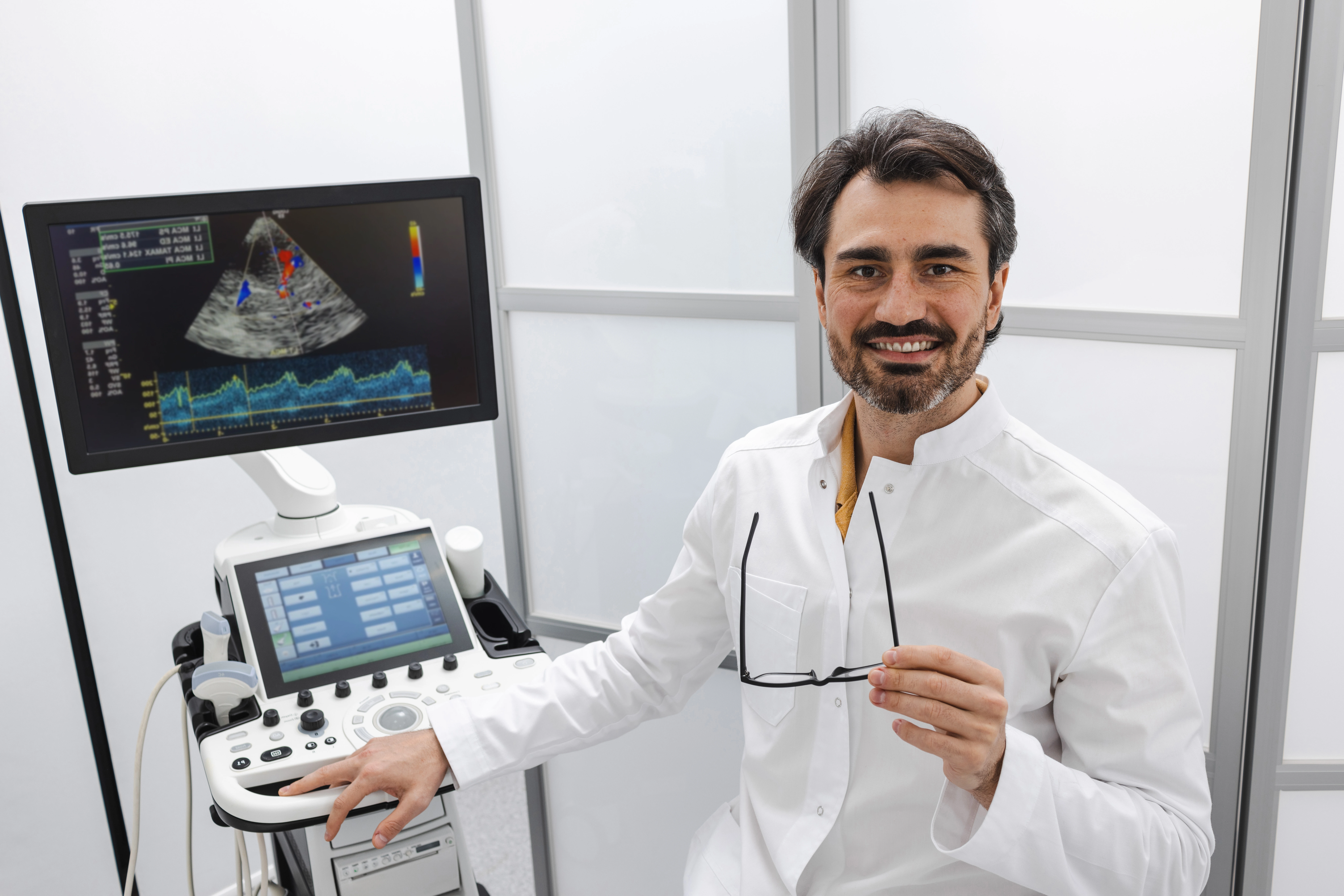 M&eacute;dico em frente a aparelho de ecocardiografia com imagem do cora&ccedil;&atilde;o exibida no monitor durante exame card&iacute;aco.