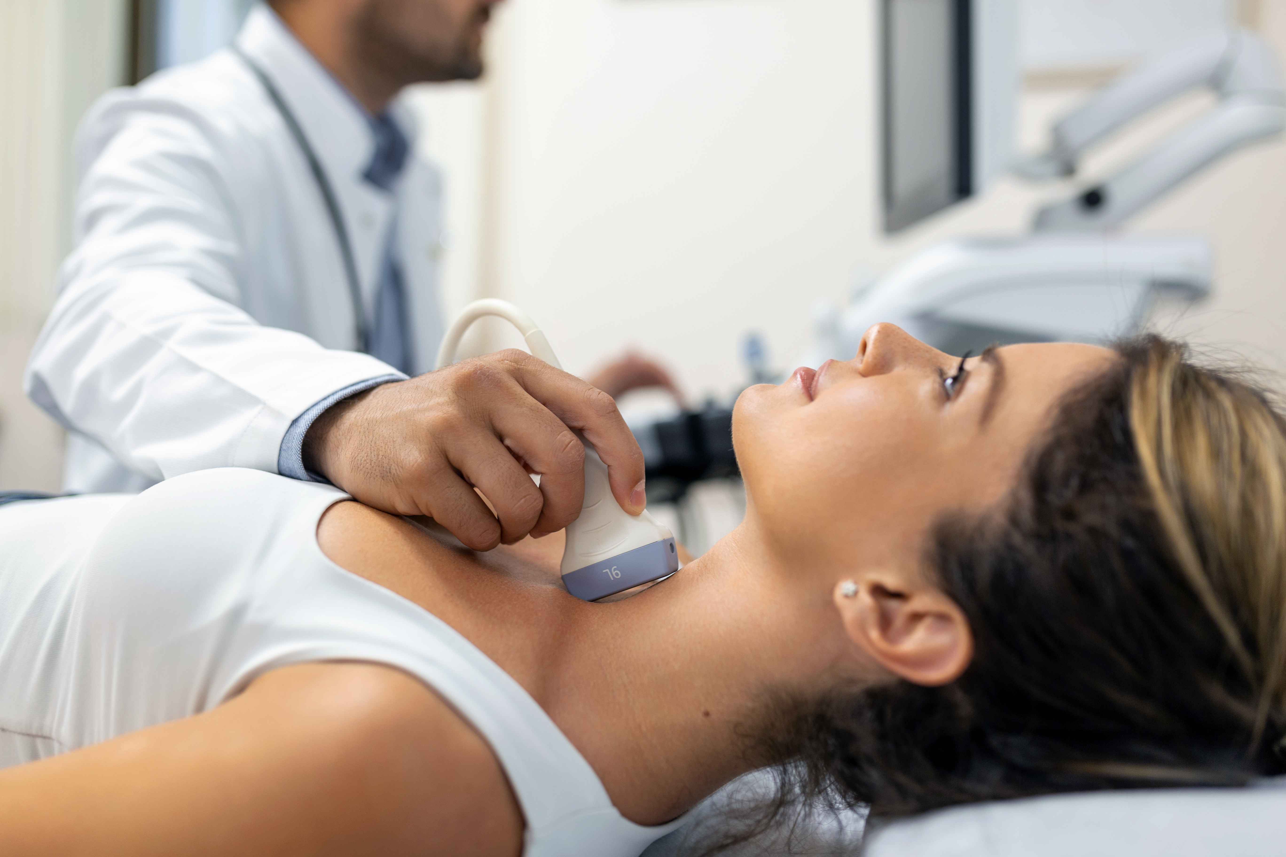 Jvem mulher tendo o pesco&ccedil;o examinado por um m&eacute;dico com um aparelho de ultrassom em uma cl&iacute;nica.