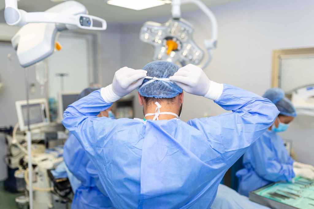 Vista traseira de um cirurgi&atilde;o do sexo masculino usando m&aacute;scara cir&uacute;rgica em uma sala de cirurgia em um hospital.